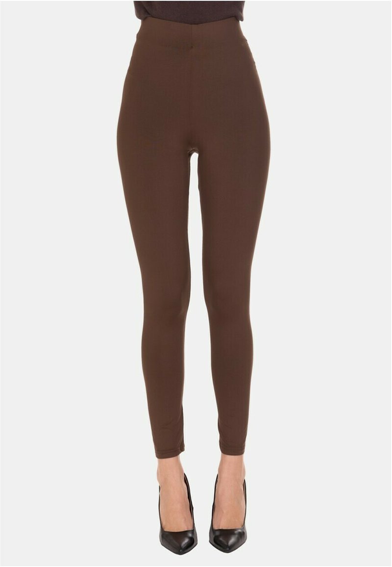 Leggings marroni a vita alta indossati con décolleté nere a punta su uno sfondo chiaro uniforme.