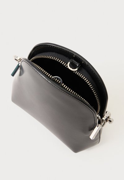 Petite pochette en cuir noir avec fermeture éclair argentée partiellement ouverte, montrant l'intérieur en tissu noir et des anneaux métalliques à l'intérieur.