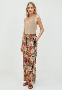 Débardeur en beige à côtes associé à un pantalon large arborant un motif de feuilles abstrait coloré et des formes géométriques. Le pantalon possède des poches latérales.