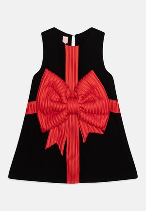 Robe noire sans manches avec un grand nœud rouge texturé et un détail de ruban vertical au centre et autour de la taille.