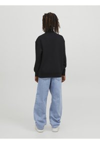 Svart oversized sweatshirt med hög hals, tillsammans med ljusblå vida jeans. Outfiten kompletteras av vita sneakers.