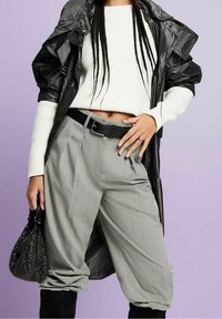 Pantaloni grigi a righe ampie, maglione bianco a costine, cappotto nero impermeabile e una borsa nera a forma arrotondata decorata con perline.