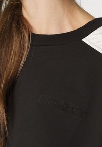 Sudadera negra con detalles en relieve blancos texturizados en los hombros y marca en relieve, con cuello acanalado y textura de tela suave.