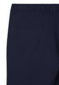 Pantaloni blu navy con vita elastica, dotati di una tasca posteriore con apertura orizzontale. Tessuto leggero e liscio con texture minimale.