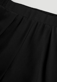 Black pleated fabric with a smooth texture, featuring an elastic waistband for comfort. Diagonal lines created by the folds add dimension.
