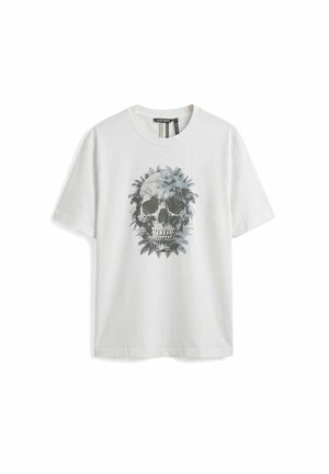 Camiseta blanca de manga corta con un diseño gráfico de una calavera rodeada de hojas de helecho en la parte frontal.