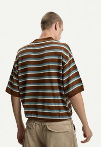 Camicia a maniche corte a righe marroni e blu con vestibilità rilassata e collo a costine, che mostra un tessuto testurizzato e dettagli di cucitura visibili.