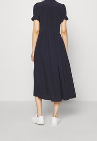 Granatowa midi sukienka z krótkimi, falbaniastymi rękawami, marszczoną talią i zwiewnym dołem. Połączona z białymi sneakersami dla uzyskania casualowego wyglądu.