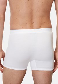 Weiße gerippte Boxershorts mit einem einfarbigen elastischen Bund und einer figurbetonten Passform, von hinten gezeigt, um die glatte Textur hervorzuheben.