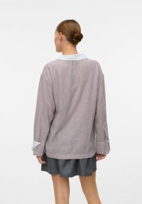 Chemise à manches longues avec des rayures verticales rouges et blanches, un col bleu clair et des accents aux poignets. Coupe décontractée et texture de tissu douce.