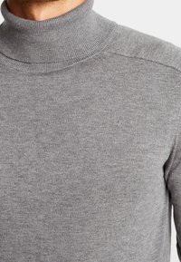 Grå turtleneck-tröja i mjukt stickat material. Har en hög krage och ribbade detaljer vid kragen och axlarna.