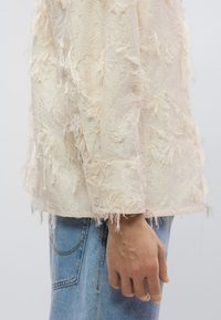 Φθαρμένο κρεμ σακάκι με υφή, που διαθέτει κουμπωτό μανίκι και λοξά κλωστές για λεπτομέρεια. Συνδυάζετ αι με ανοιχτό μπλε τζιν.