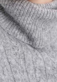 Szary dziergany sweter z wysokim, prążkowanym golfem i teksturowanym wzorem. Tkanina wydaje się miękka i ciepła, z wizualnie wypukłym przeszyciem.