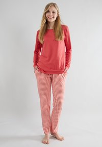 Chemise à manches longues rouge associée à un pantalon de pyjama à carreaux rouges et blancs. L'ensemble présente une coupe décontractée et un tissu doux. Pas de motifs visibles sur le haut.