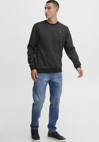 Dunkelgrauer Sweatshirt mit strukturiertem Finish, Rundhalsausschnitt und gerippten Bündchen. Kombiniert mit hellblauen Jeans und schwarzen Turnschuhen.
