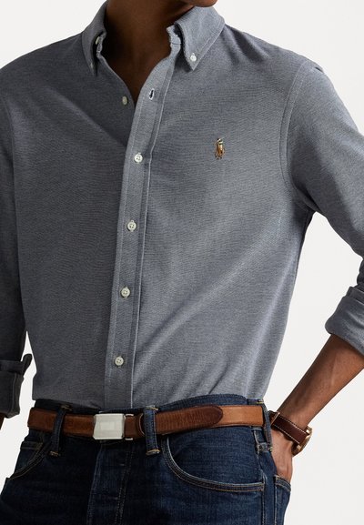 Cotton button-down shirt in navy blue with a subtle herringbone pattern. Features a small embroidered logo and a collared neck.