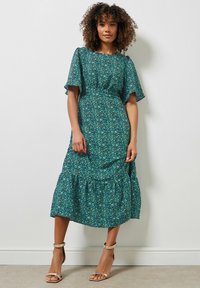 Grøn blomster midi-kjole med korte flæseærmer, lagdelt skirt og en indsnævret talje. Mønsteret har små pink og hvide blomster.