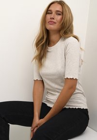 Harmaa ribbitekstiili t-paita, jossa on aaltoilevat lyhyet hihat, tiukka muotoilu, yhdistetty mustiin farkkuihin. Neutraali, teksturoitu vaate.