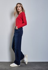 Rotes Langarmoberteil, kombiniert mit dunkelblauen weit geschnittenen Jeans und weißen Sneakern, hat ein klassisches Design und eine glatte Stoffoberfläche.