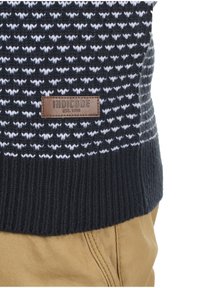 Marineblå og hvid mønstret sweater med ribbet tekstur, der har en brun rektangulær læderlap mærket "INDICODE EST. 1993."