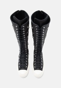 Botas de cano alto pretas com frente laceada, orifícios prateados e sola branca de borracha. A parte superior apresenta uma textura suave e um design estruturado.