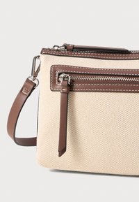 Borsa in tela beige con accenti in pelle marrone, dotata di tasca frontale con zip, cinturino regolabile e dettagli di cucitura a contrasto.