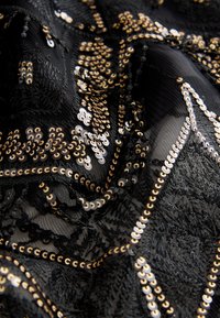 Black fabric featuring intricate patterns of gold and silver sequins, textured with varying surface depths, creating visual interest.
