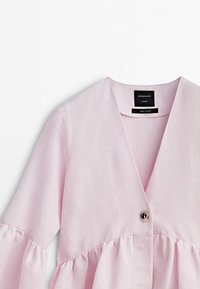 Blouse en lin rose clair avec un col en V, des manches trois-quarts en forme de cloche, une taille froncée et un seul détail en métal au niveau du bouton. Étiquette visible à l'intérieur.