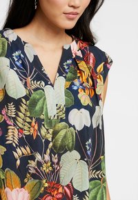 Tunic floreale con sfondo navy e foglie e fiori vivaci nei colori verde, rosa e giallo. Design a V con maniche corte.