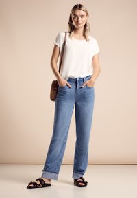 Camiseta blanca de manga corta, corte relajado, combinada con jeans de tiro alto en azul claro, con dobladillo en el tobillo, y sandalias negras con estampado de leopardo.