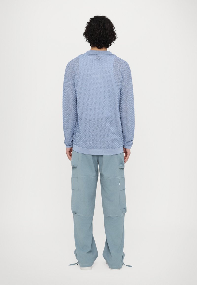 Maglione azzurro chiaro con texture, collo rotondo e maniche lunghe, abbinato a pantaloni cargo azzurro chiaro con tasche laterali e polsini elasticizzati.