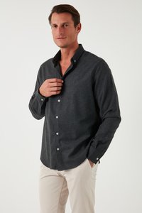 Camisa de botón gris oscuro con cuello, que presenta una tela texturizada y botones blancos, combinada con pantalones de color claro.