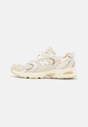 Crème en beige New Balance 530 sneaker met mesh- en lederen details, zichtbare veters en dikke gevoerde zool op een witte achtergrond.