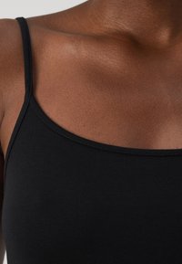 Black tank top with thin straps, made of smooth fabric. Features a rounded neckline and a fitted design. Soft texture visible.