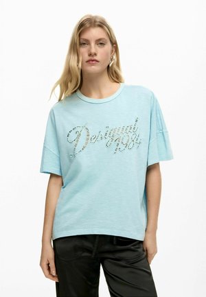 T-shirt oversize azzurro chiaro in tessuto morbido, con grafica lucida "Desigual 1984" in corsivo sul davanti. Maniche corte.