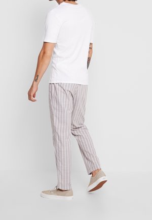 T-shirt blanc à manches courtes, pantalons rayés gris clair et baskets beiges. Les pantalons ont des rayures verticales et une coupe décontractée.
