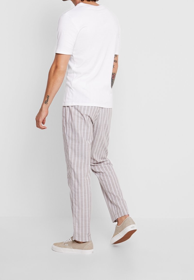 Camiseta blanca de manga corta, pantalones rayados en gris claro y zapatillas beige. Los pantalones presentan rayas verticales y un corte relajado.