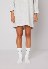 Vestido de algodón gris de manga larga, con dobladillo asimétrico, combinado con calcetas blancas hasta la mitad de la pantorrilla que presentan texto azul "American Vintage". Look sencillo y casual.