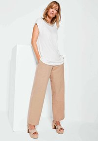 Weißes kurzärmeliges Oberteil mit rundem Ausschnitt, kombiniert mit beigen weiten Hosen und sandfarbenen Blockabsatzsandalen. Glattes Material und lässige Passform.