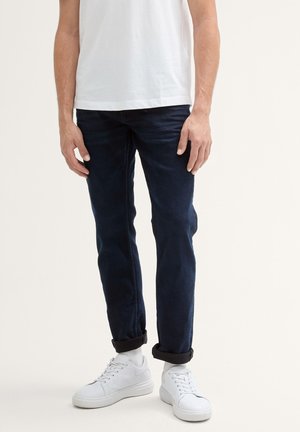 Jeans de mezclilla azul oscuro con un corte ajustado, que cuentan con puños enrollados y una textura suave. Combinados con zapatillas bajas blancas.