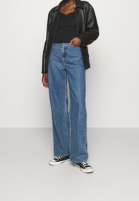 Giacca in pelle nera, top nero e jeans a gamba larga blu con vita alta, abbinati a sneakers bianco e nere. Texture lisce, stile casual.
