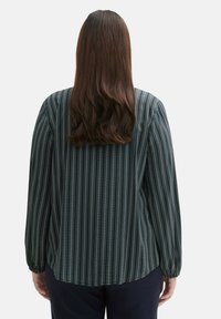 Cămașă cu mânecă lungă de culoare albastră închisă, cu dungi verticale subțiri și accente albe subtile. Are o croială lejeră și manșete strânse.