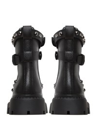 Botas de tobillo negras con un acabado de cuero texturizado, correas con tachuelas y suelas de goma gruesas. Presentan un detalle de hebilla en la parte trasera y una suela con un diseño resistente.
