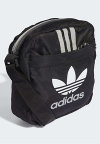 Borsa a tracolla nera in nylon con tracolla regolabile, dotata di un grande logo bianco Adidas e tre strisce grigie lungo la parte superiore.