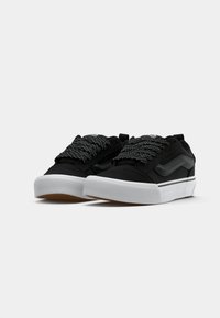 Sorte kanvas-sneakers med strukturert overdel, hvit gummisåle og spraglete svart-hvite lisser. Har sidemerkelogo og polstret tunge.