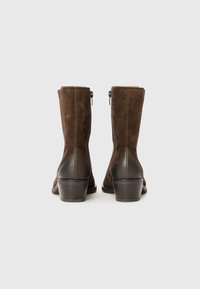 Stivaletti alla caviglia in suede marrone con tacco in pelle liscia, chiusura con zip e tacco leggermente svasato. Design strutturato con rifiniture pulite.