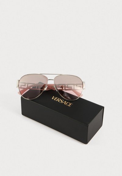 Ochelari aviator cu lentile roz și ramă argintie așezați pe un etui Versace negru cu litere aurii.