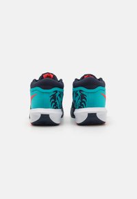 Turkoise sneakers met marineblauwe accenten en rode highlights. Textuurmateriaal heeft leeuwgraphics aan de zijkanten en een witte outsole.