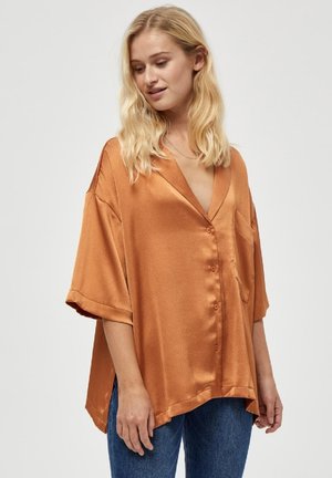 Satin kastanjebruine shirt met korte mouwen, een losse pasvorm, een v-hals en een enkele borstzak, gecombineerd met blauwe jeans.