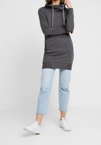 Szary tunikowy płaszcz z kapturem, z białymi sznurkami i dwoma bocznymi kieszeniami, połączony z jasnoniebieskimi, krótkimi dżinsami i białymi trampkami.